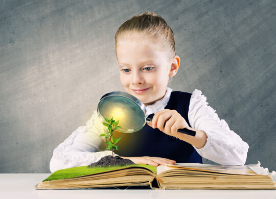Schoolgirl examining opened book with magnifying glass