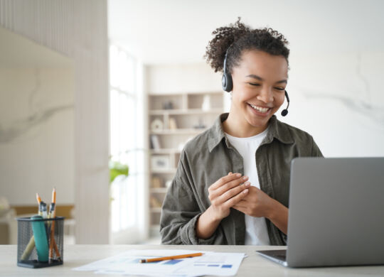 Happy student has online lesson from home. Distance study on quarantine. Young woman in headset gives consultation. African american manager is smiling. Remote work of an operator of support service.